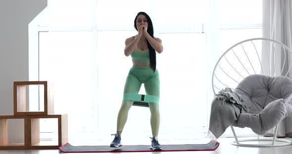 Resistance band fitness girl in sportswear doing leg workout floor exercises.