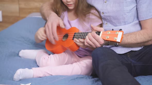 Young Caucasian Man Teaching Guitar and Ukulele to His Daughter Learning