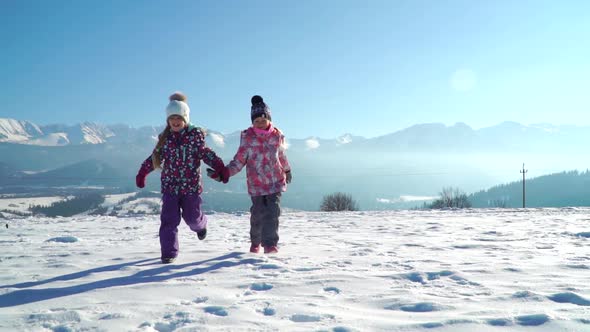 Charming Kids in Outwear Running on Snowy Terrain with Beautiful Mountains on Background in Sunshine