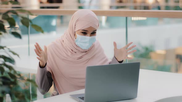 Surprised Arab Woman Wearing Medical Mask Looking at Laptop Screen Receiving Email Reading Good News alt
