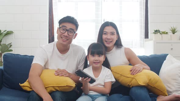 Dad, mom and daughter watching TV together and having fun lying on sofa in living room. alt