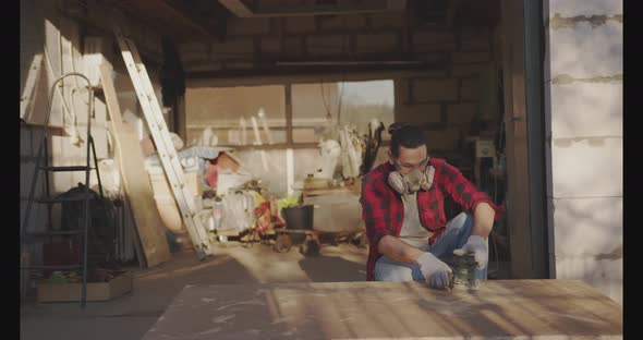 A Man in a Respirator Goggles Polishes a Parquet Board with an Orbital Sander alt