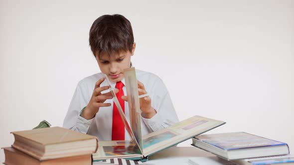Curious School Kid in Red Tie Sitting at Table Folding Pages of Geographic Atlas with Interest on alt