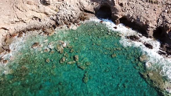 Aerial View of a Cave with Crystal Clear Waves at a Rocky Coast with Clear Blue Water