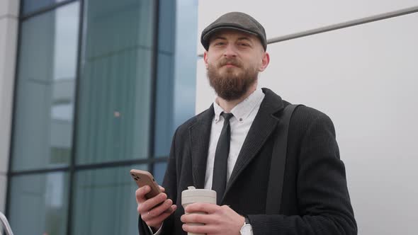 A Man in a Suit Looks at the Phone and Then at the Camera Holding a Coffee Cup