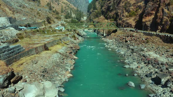 Beautiful Bhagirathi River flowing through small rocks under small green bridge