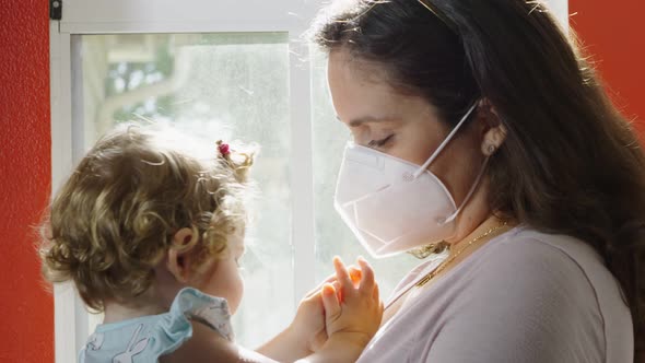 Baby Girl Looking at Mother Who Is Wearing a Protective Mask alt