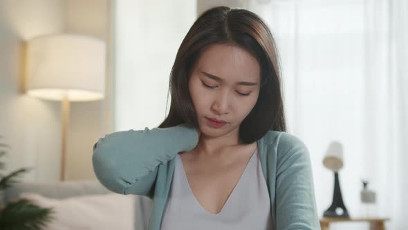 Tired Pretty Asian woman sitting in a living room feeling exhausted and having neck pain