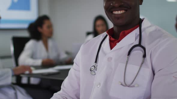 Portrait of african american male doctor sitting in meeting room looking to camera smiling alt
