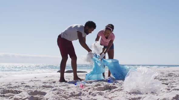 African american couple collecting plastic waste on the beach alt