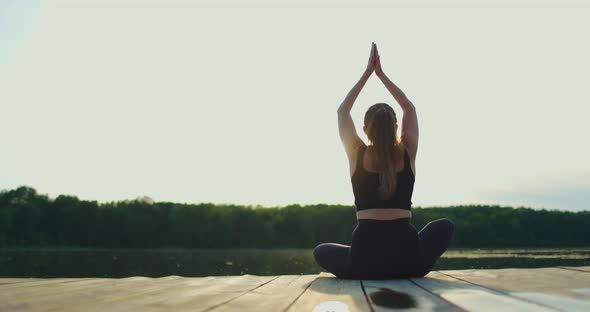 Young Woman with Her Hands Raised Practices Yoga By the Lake alt