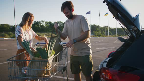 Girl and Guy Smiling Taking Groceries Out of Cart and Putting It Into Car alt