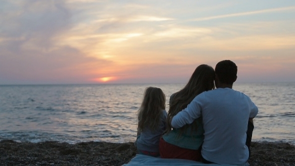 Happy Family Sitting In The Sunset Near The Sea In