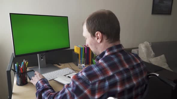 Disabled Man Sitting in a Wheelchair Working at a Computer with a Green Screen