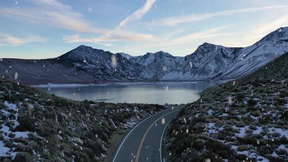 Beautiful mountain road with reveal of lake during winter season and snowfall, aerial ascend view alt