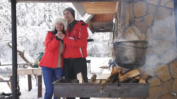Young Happy Couple on a Winter Day is Prepared in the Courtyard of a Wooden Forest House on an Open alt