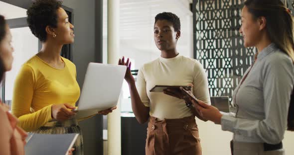 Group of diverse businesswomen using laptop and tablets and talking in office alt