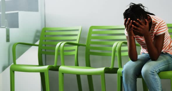 Upset girl sitting on chair in hospital corridor alt