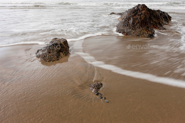 Water rushes around rocks on beach.