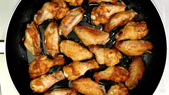 Many Crispy Fried Chicken Wings Pieces in Frying Pan Turning Slowly on Turntable alt