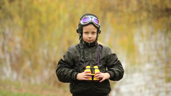 Cute little girl in a pilot's helmet and glasses looking through binoculars in the autumn Park
