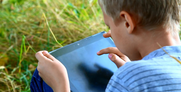 Child Playing Computer Games on Tablet pc in Park