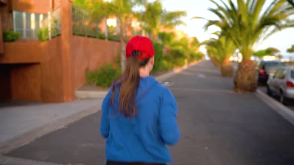 Woman Runs Down the Street Among the Palm Trees at Sunset Back View alt