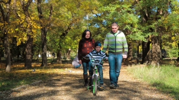 Happy Young Family With A Child On Bike Walking In