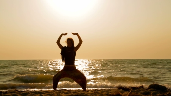 Young Woman Doing Yoga On Sandy Beach At Sunset