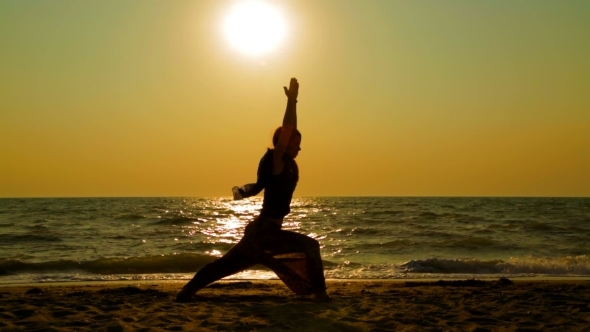 Woman Practicing Yoga On The Beach At Sunset
