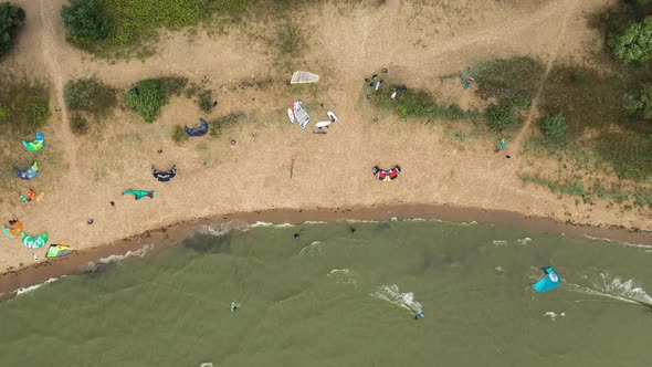 AERIAL: Top View of the Beach Filled With Kite Surfers Preparing to Kite on a Green Colour Sea alt