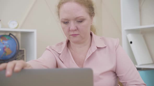 Senior Redhead Woman Closing Laptop and Looking at Camera. Lady Expressing Opposite Emotions alt