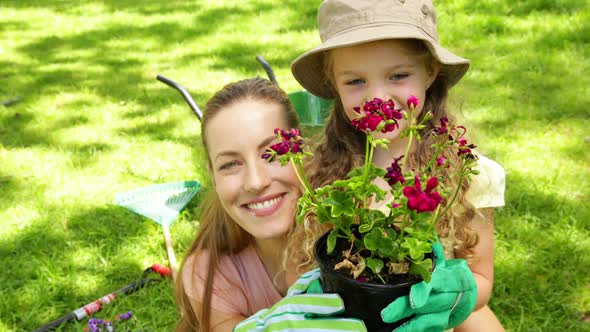 Cute Little Girl Holding Pot Of Flowers With Her Mother alt