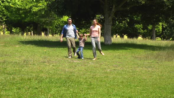 Little Boy And Parents Running Towards Camera In The Park Holding Hands alt