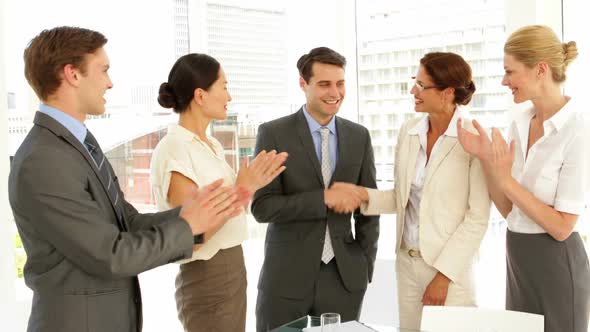 Business People Shaking Hands At Interview While Others Clap alt