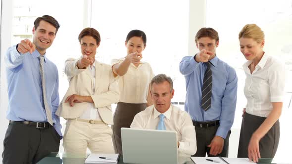 Business Team In Front Of Laptop Then Pointing To Camera alt