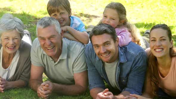 Multi Generation Family Smiling And Lying On Ground In A Park alt
