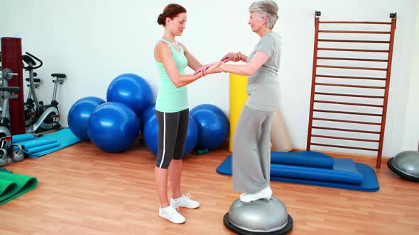 Trainer Helping Elderly Client To Use Bosu Ball alt