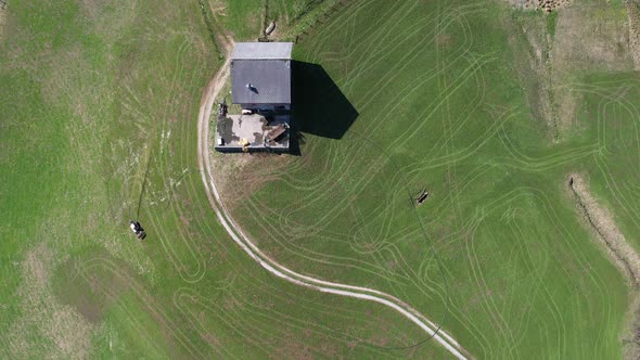 Top down aerial view, Mountain farmer tills his field with tractor and hose. alt