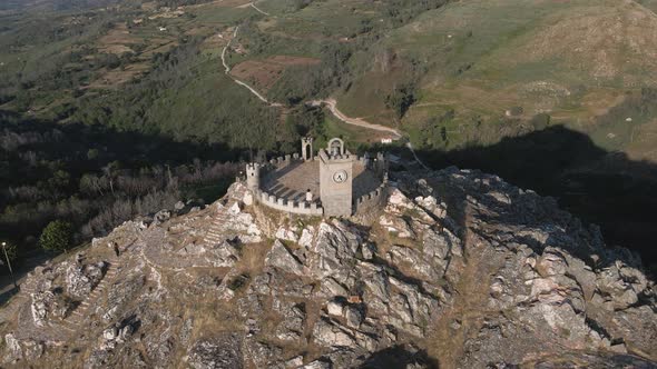Tourist stands on the towers of the Folgosinho Castle as a drone circle at sunset. alt