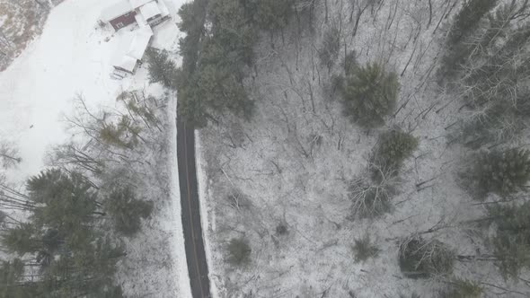 Top down view of winter road in Wisconsin through farm field with buildings and creek.