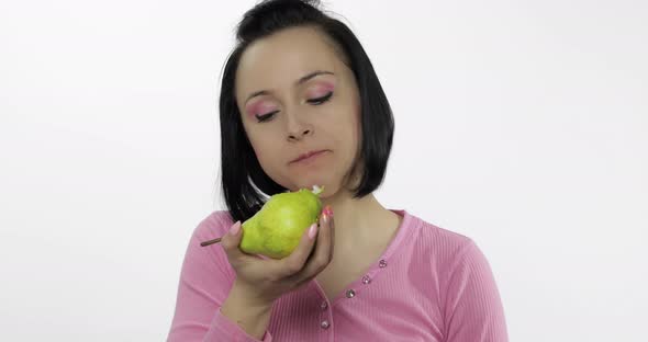 Young Beautiful Woman Eating Big, and Juicy Green Pear on White Background alt
