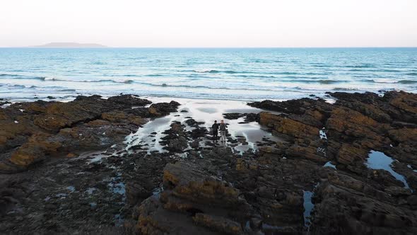 Two young people at a rocky beach in malahide. They are looking at the incoming waves. alt