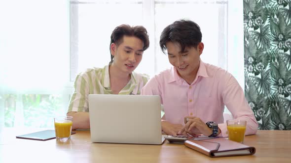 Attractive male lgbtq collegues working together with using laptop pc and paper showing chart alt