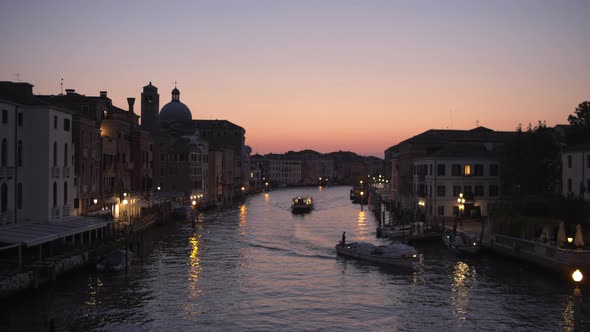 Wide static shot of boats cruising through Canal Grande at Twilight, Venice, Italy alt
