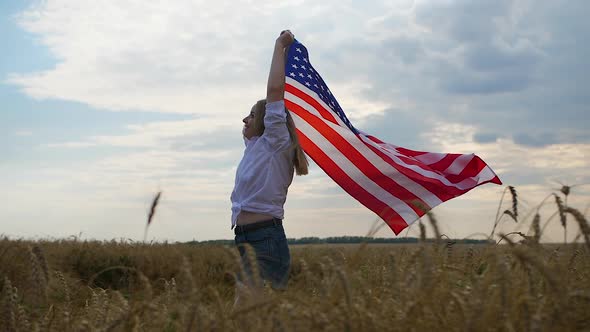 Happy Patriotic Young Woman Waves the US Flag and Jumps Into the Field