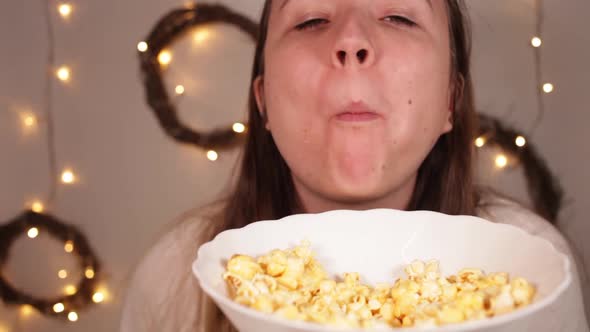 Woman Eats Popcorn Christmas Lights on a Blury Background A Woman with a Huge Popcornfull Mouth