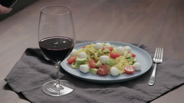 Slow Motion Pour Red Wine Into Wineglass with Bowl of Fettuccine on Background alt