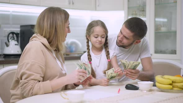 Joyful Caucasian Young Family Scattering Money in Slow Motion Resting in Kitchen at Home alt