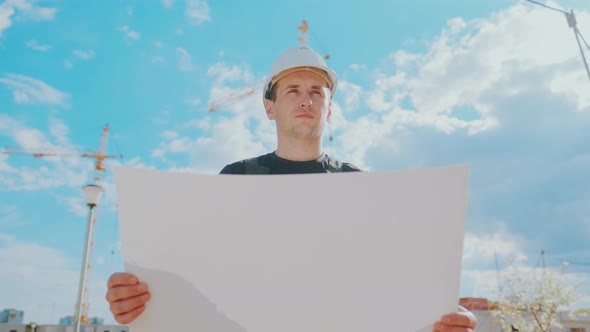 A Man in a Helmet Is Holding a Construction Plan in His Hands. A Builder Is Checking Blueprints.